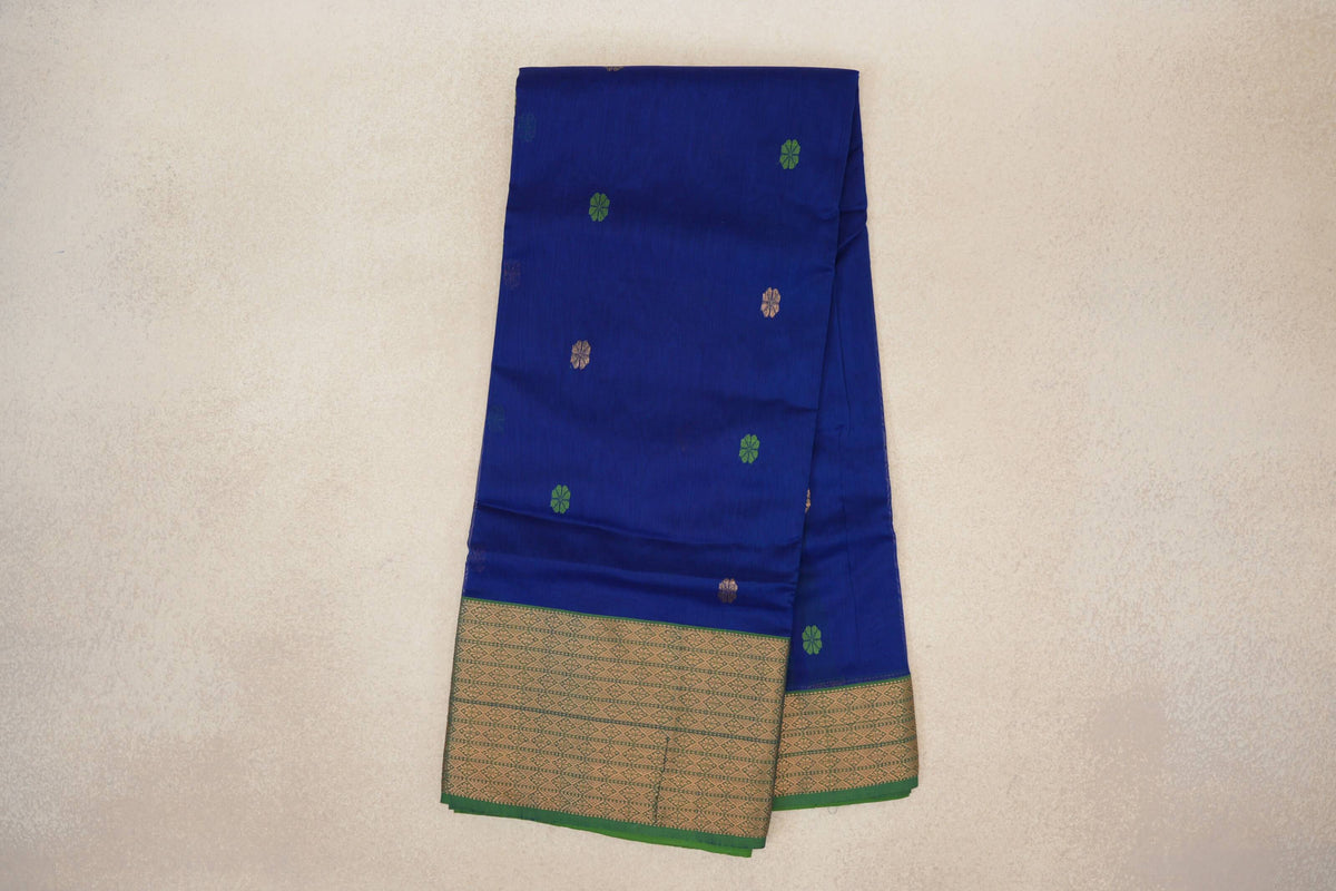 Folded Maheshwari silk cotton saree with a deep royal blue body, scattered green and gold motifs, and a patterned gold border edged in forest green.