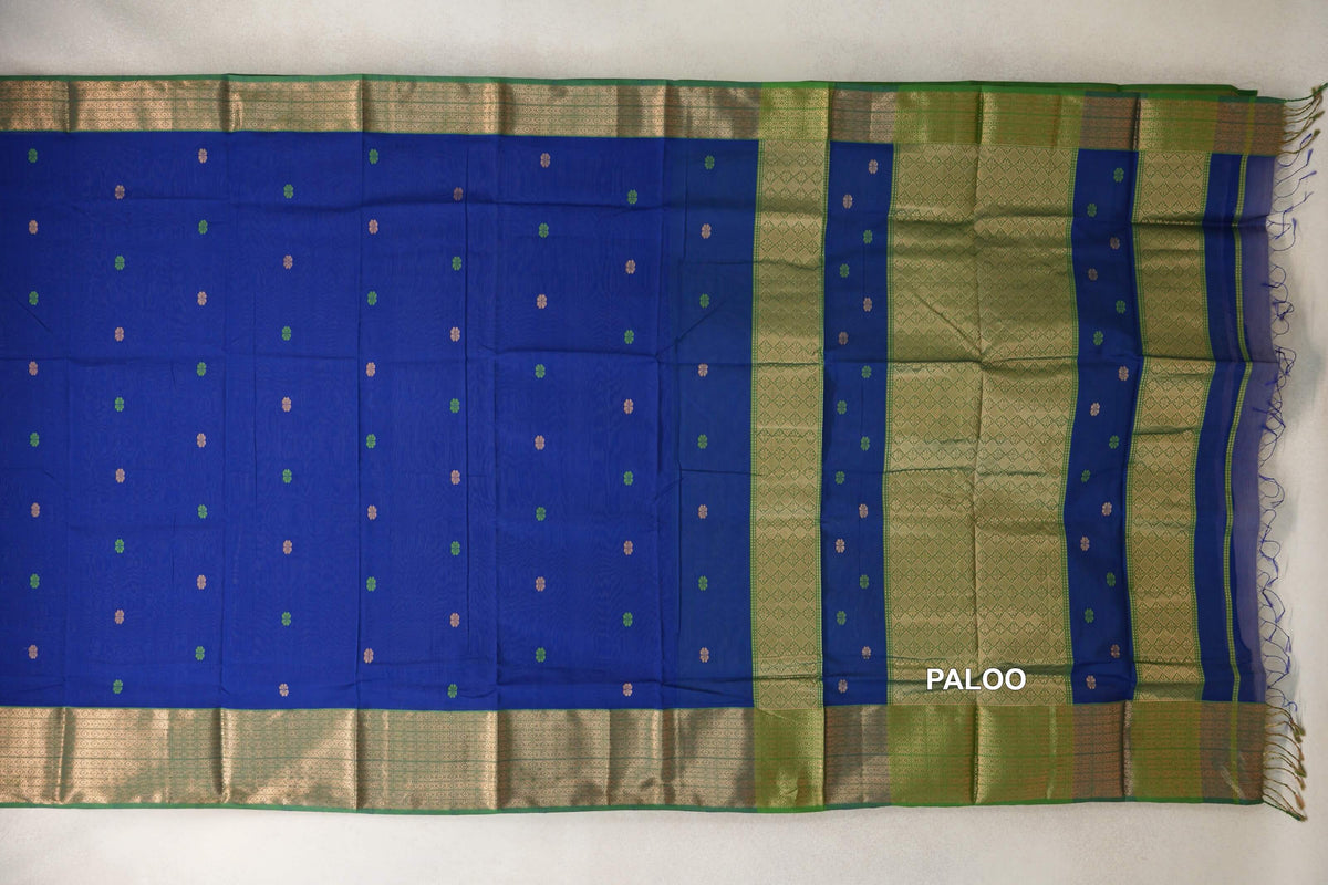 Maheshwari silk cotton saree laid flat, with a deep royal blue body, small scattered motifs, forest green patterned borders and pallu, and fringe.