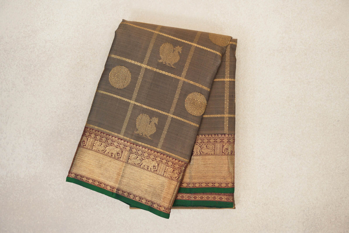 Folded olive green Kanjivaram silk saree with gold checks, bird and circular motifs, and a deep maroon patterned border edged in bottle green.