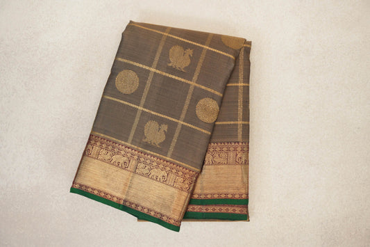Folded olive green Kanjivaram silk saree with gold checks, bird and circular motifs, and a deep maroon patterned border edged in bottle green.