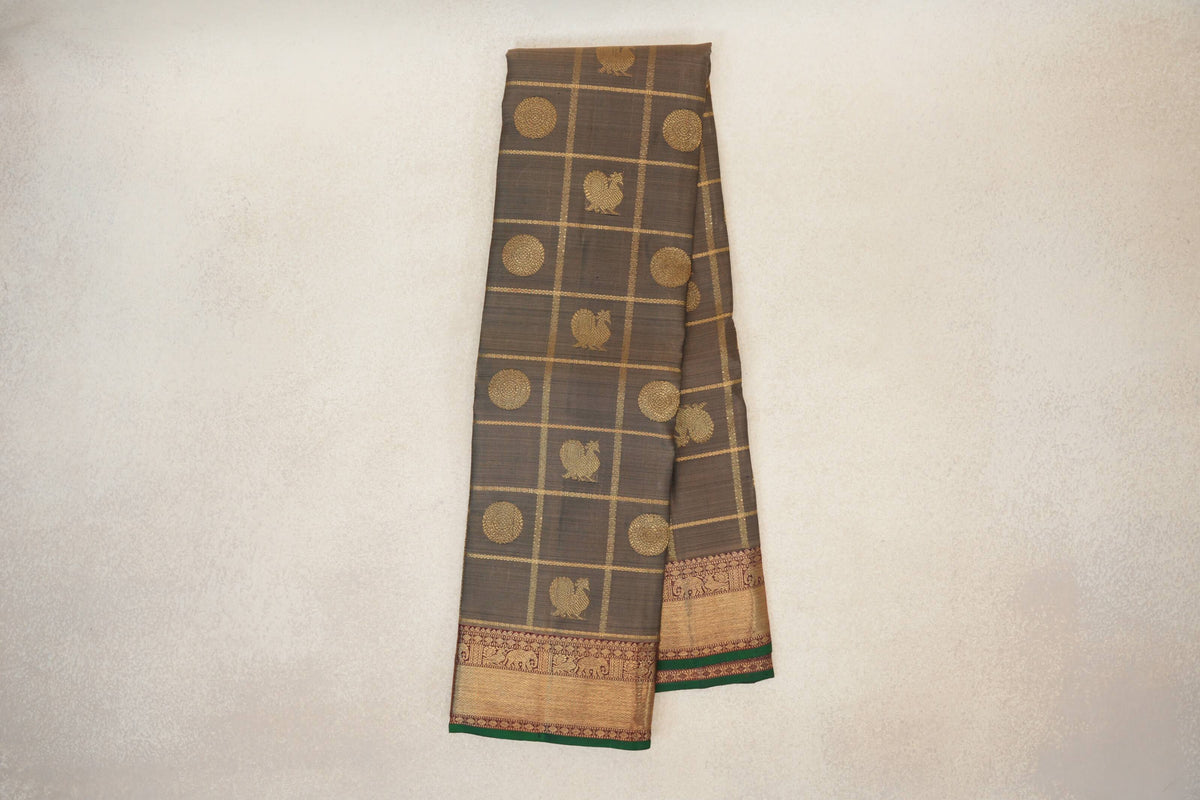 Folded olive green Kanjivaram silk saree with gold checks, bird and circular motifs, and deep maroon borders edged in bottle green.