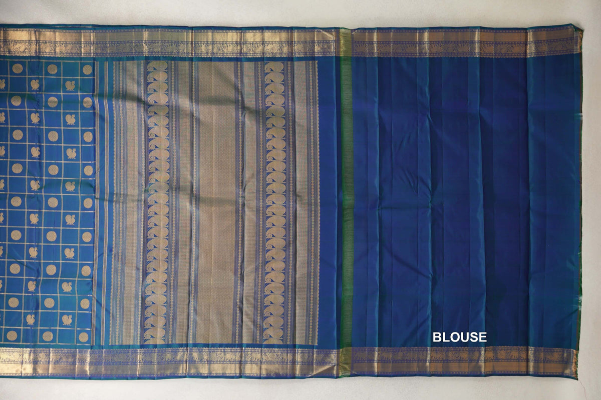Peacock blue Kanjivaram silk saree laid flat, showing a checked body with gold-toned motifs, a striped pallu, ornate borders and matching blouse fabric.