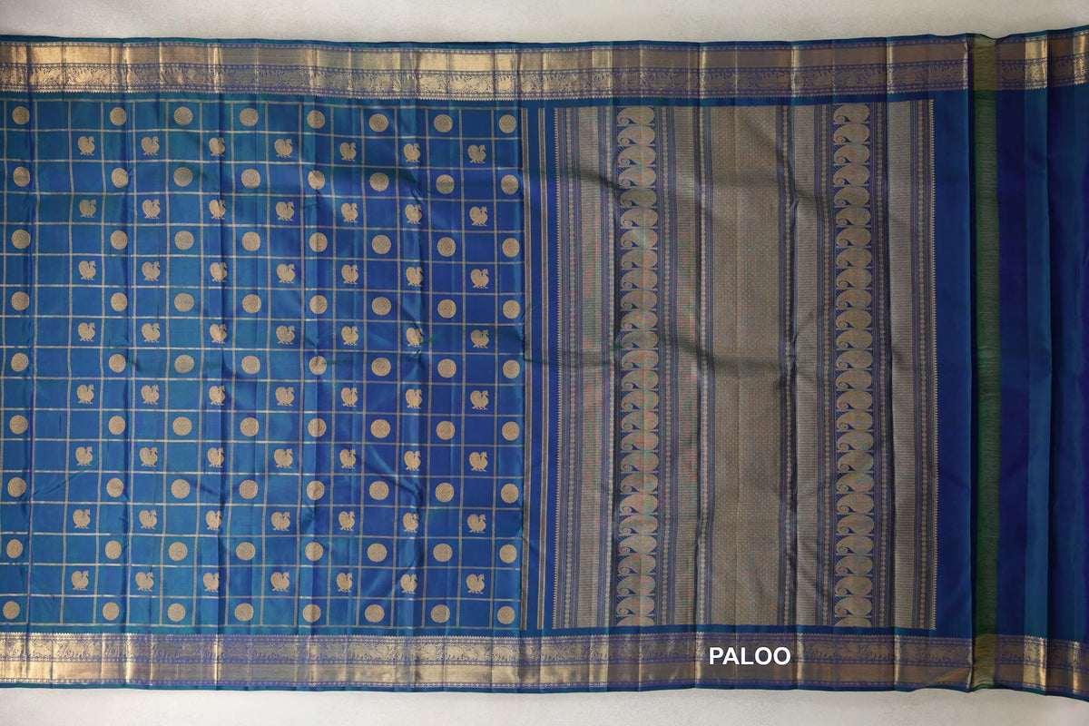 Peacock blue Kanjivaram silk saree laid open, showing a checked body with gold circles and small motifs, ornate borders and a striped pallu.