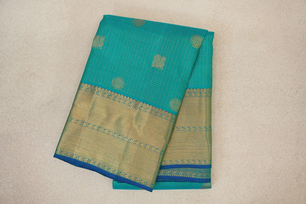 Folded aqua green Kanjivaram silk saree with fine zari checks, scattered gold motifs and a broad gold woven border edged in blue.