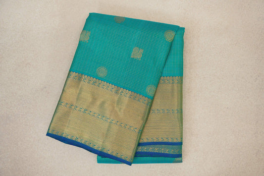 Folded aqua green Kanjivaram silk saree with fine zari checks, scattered gold motifs and a broad gold woven border edged in blue.