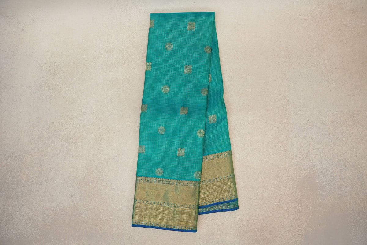 Folded aqua green Kanjivaram silk saree with fine zari checks, scattered gold motifs and a broad gold border edged in blue.