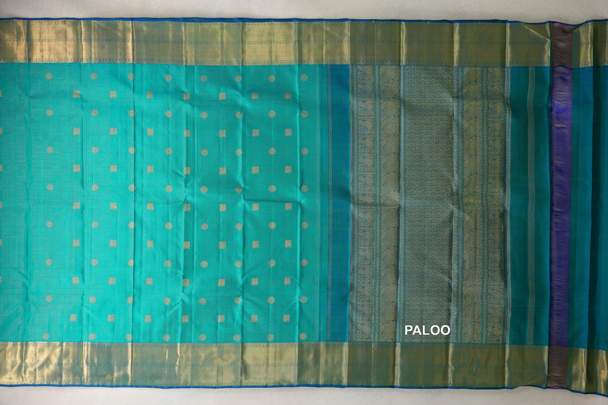 Aqua green Kanjivaram silk saree laid open, with fine zari checks, gold dots and squares, wide gold borders and an ornate pallu.