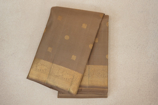 Folded greenish beige Kanjivaram silk saree with fine horizontal lines, scattered gold motifs and an ornate gold zari border.