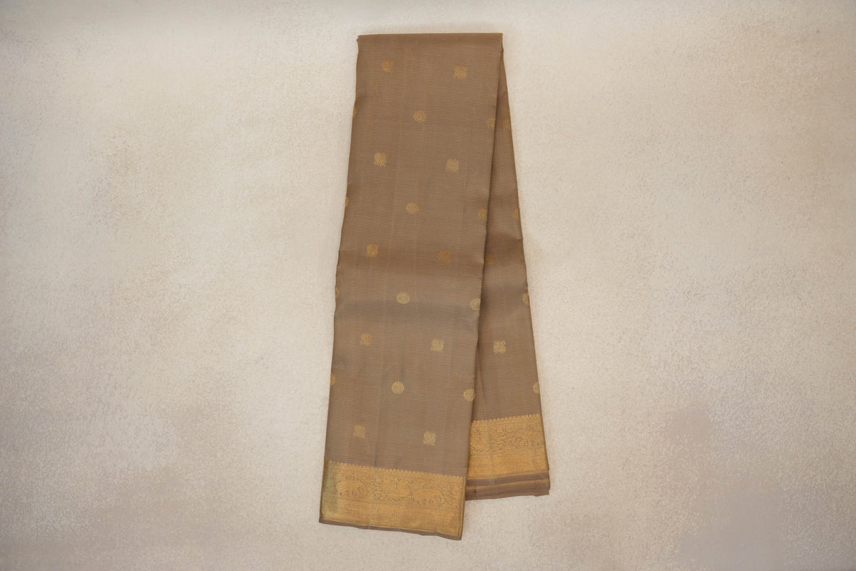 Folded greenish beige vintage Kanjivaram silk saree with scattered gold motifs and an ornate gold border along the lower edge.