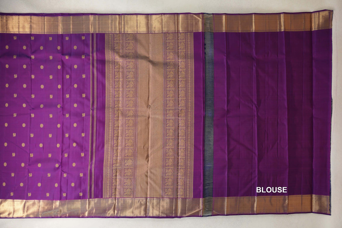 Purple Kanjivaram silk saree laid flat, showing a gold-motif body, ornate gold pallu, wide gold borders and a purple blouse piece.