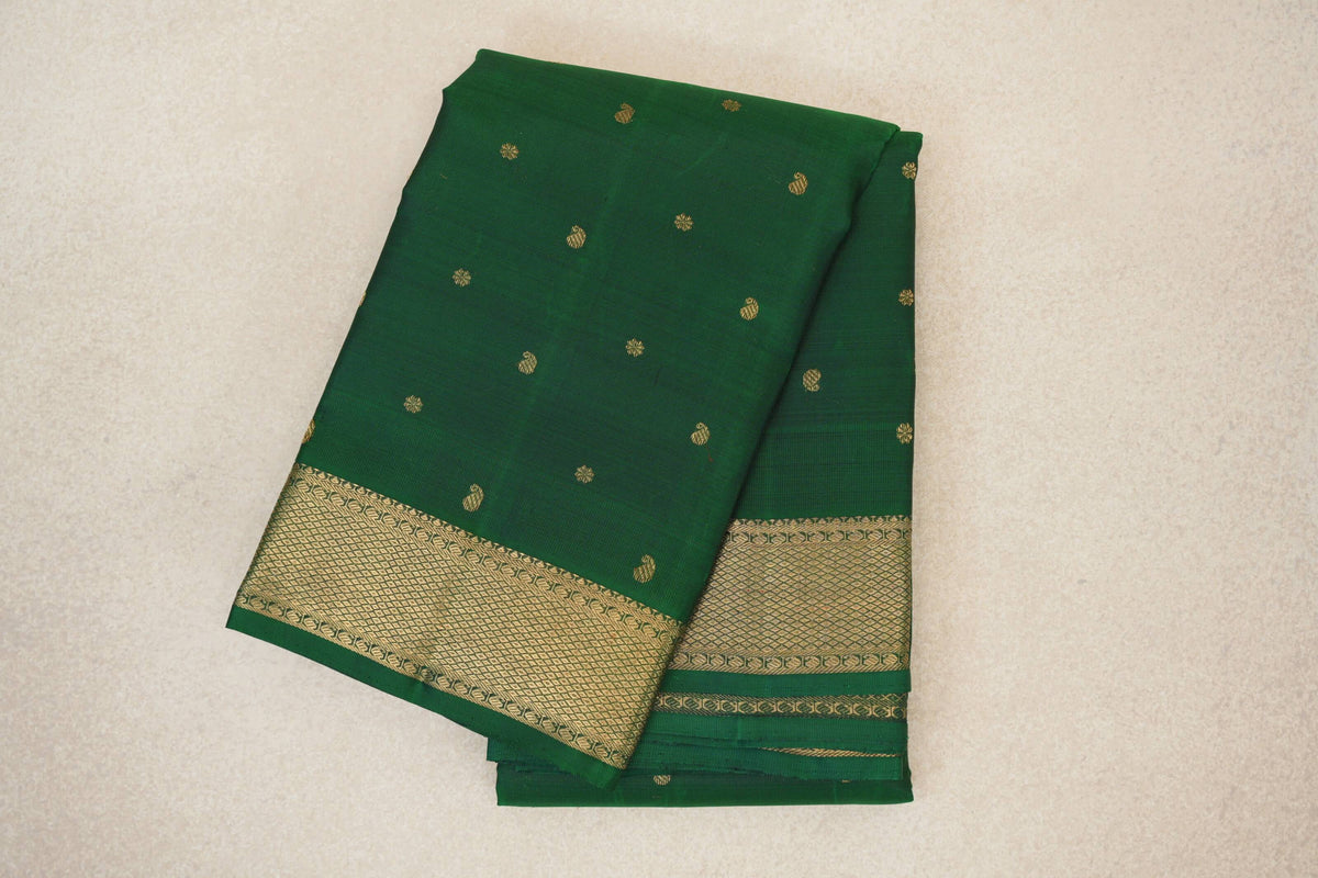 Folded bottle green Kanjivaram silk saree with scattered gold motifs and a wide gold geometric border.