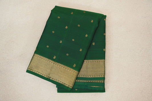 Folded bottle green Kanjivaram silk saree with scattered gold motifs and a wide gold geometric border.