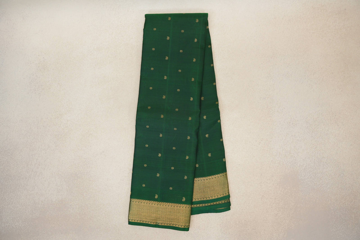 Folded bottle green Kanjivaram silk saree with scattered small gold motifs and a broad gold lattice-patterned border.