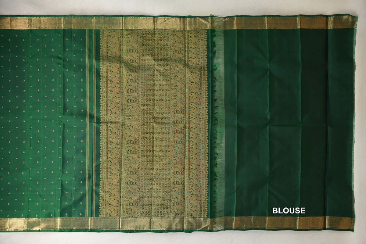 Bottle green Kanjivaram silk saree laid out with a dotted body, ornate gold zari pallu, broad borders and a matching blouse piece.