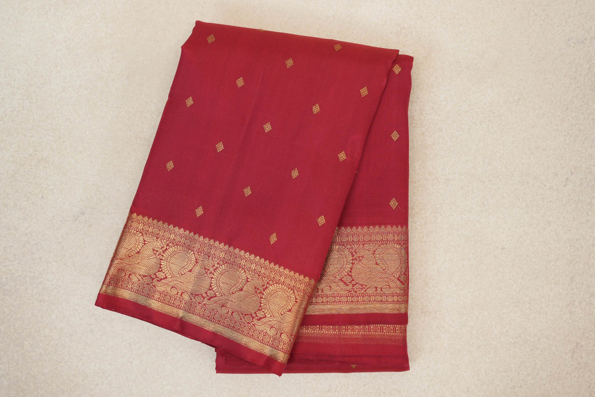 Folded crimson red silk Kanjivaram saree with scattered small gold diamond motifs and a wide gold paisley-patterned border.