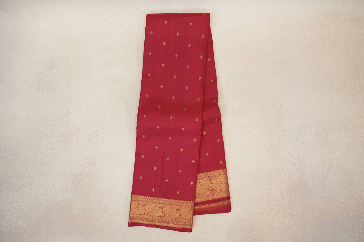 Folded crimson red Kanjivaram silk saree with scattered gold diamond motifs and a wide gold border featuring peacock designs.
