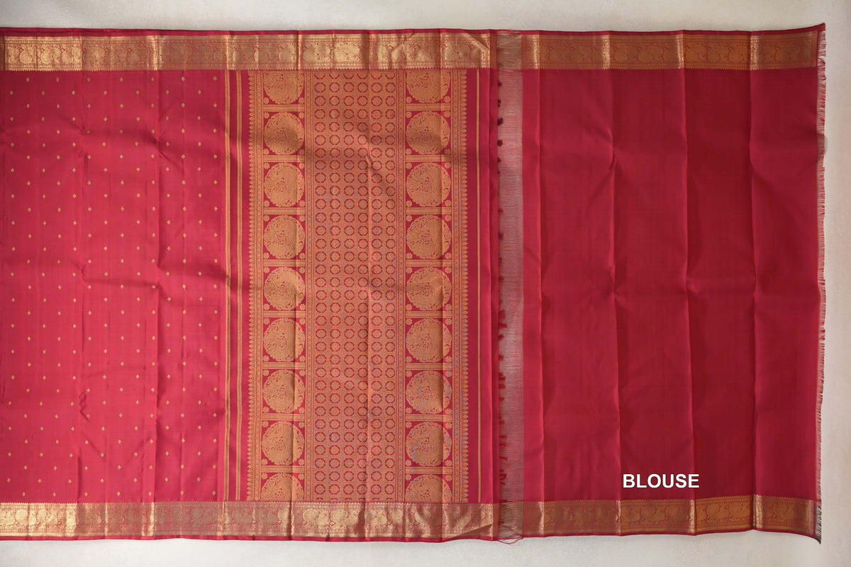 Crimson red Kanjivaram silk saree spread out, showing a dotted body, gold-patterned pallu and borders, and matching blouse fabric on the right.
