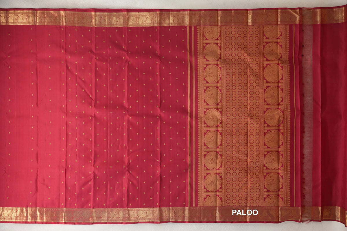 Crimson red silk Kanjivaram saree spread open, with small gold motifs across the body, ornate gold borders and a pallu with circular designs.