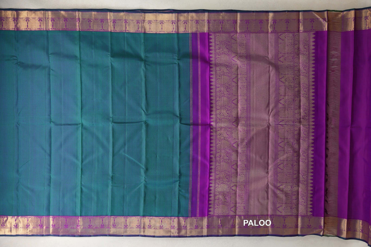 Spread-out peacock green Kanjivaram silk saree with purple and gold-toned borders, an ornate purple pallu and bottle green selvedge.