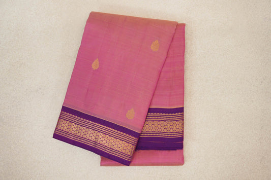Folded rose pink Kanchipuram silk saree with scattered gold leaf-like motifs and a purple border with gold geometric bands.