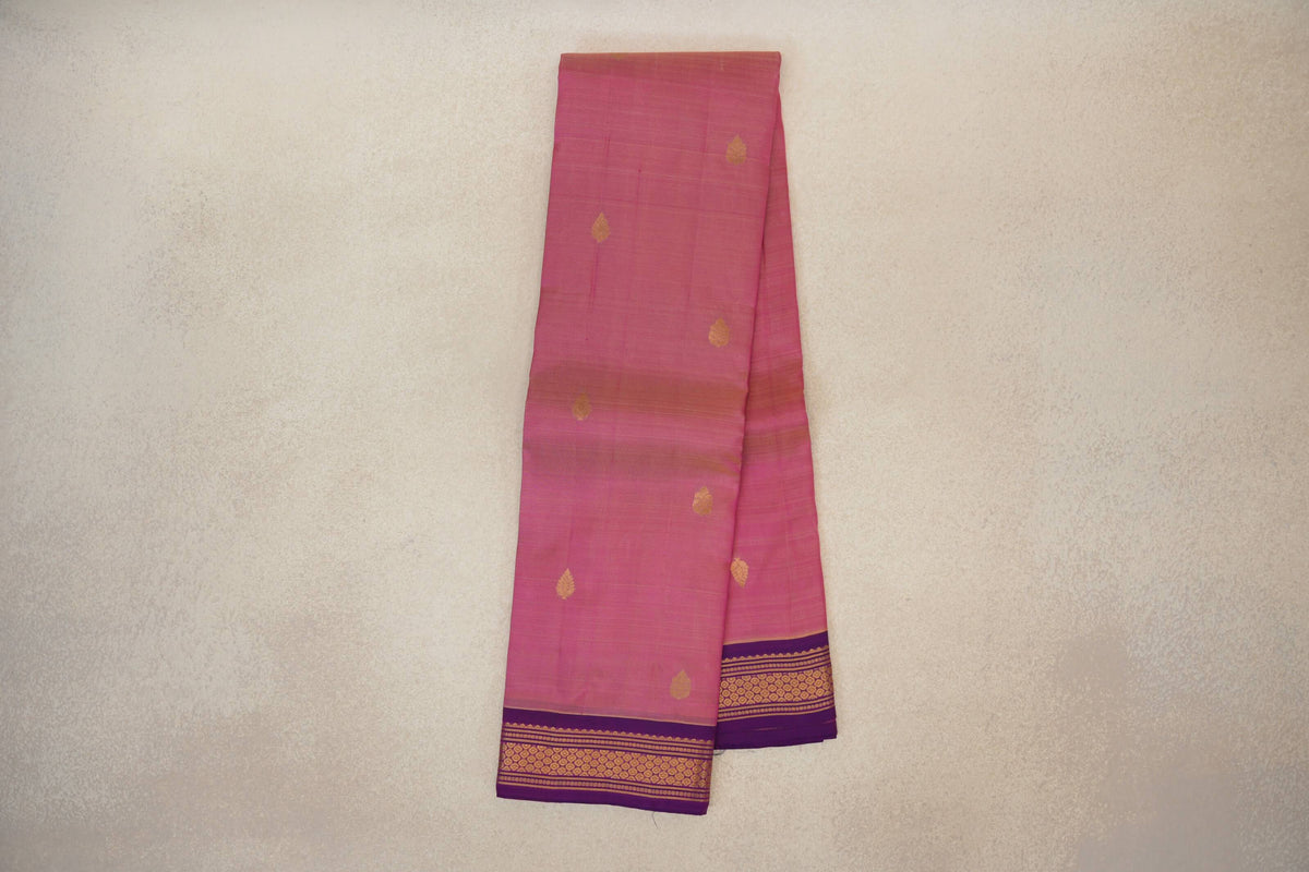 Folded rose pink lightweight Kanchipuram silk saree with scattered gold leaf motifs and a purple border patterned in gold.