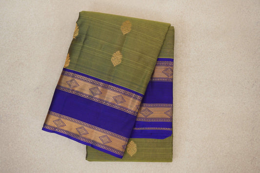Folded olive green Kanchipuram silk saree with scattered gold motifs and royal blue borders featuring gold diamond-patterned bands.
