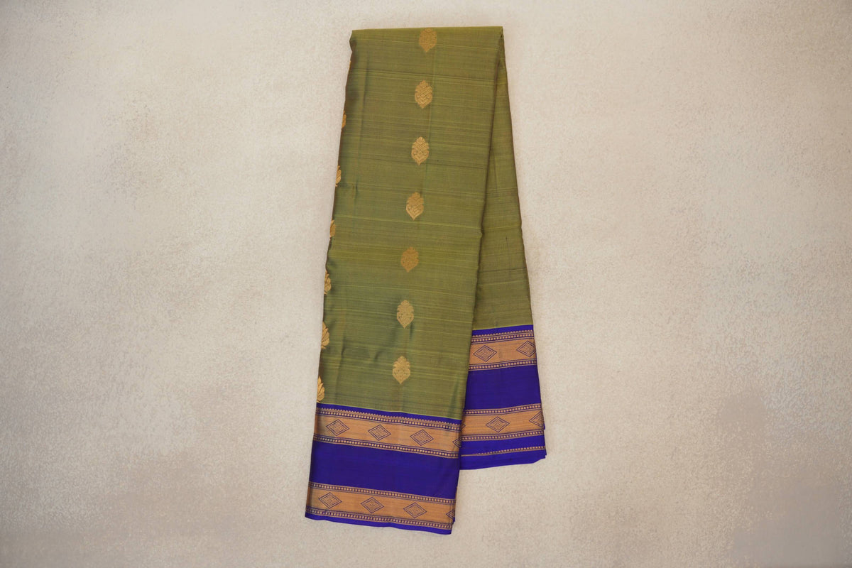 Folded olive green Kanchipuram silk saree with scattered gold motifs and royal blue borders featuring gold diamond-patterned bands.