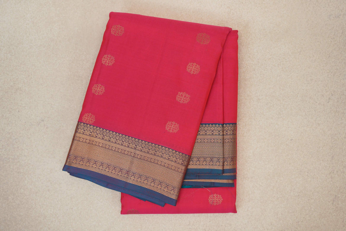 Folded lightweight Kanchipuram silk saree in bright rani pink, with spaced gold floral motifs and a teal blue border with intricate gold patterns.