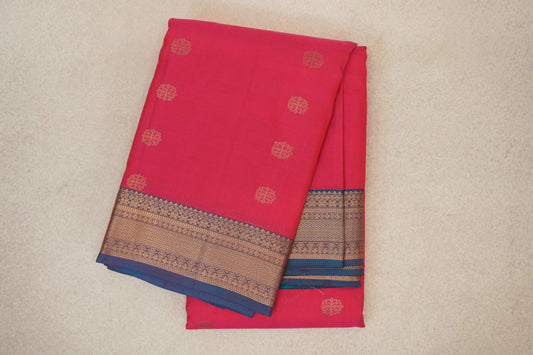 Folded lightweight Kanchipuram silk saree in bright rani pink, with spaced gold floral motifs and a teal blue border with intricate gold patterns.