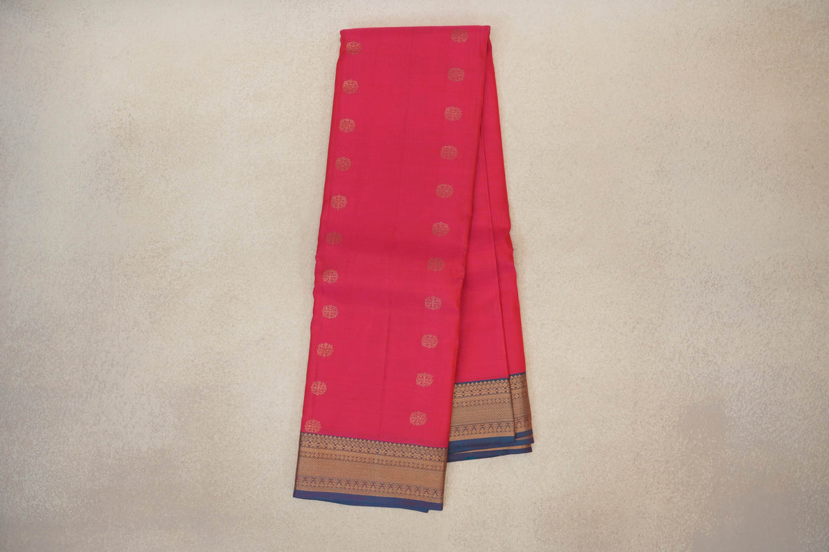Folded light weight Kanchipuram silk saree in bright rani pink, with small gold motifs and a patterned gold border edged in teal blue.