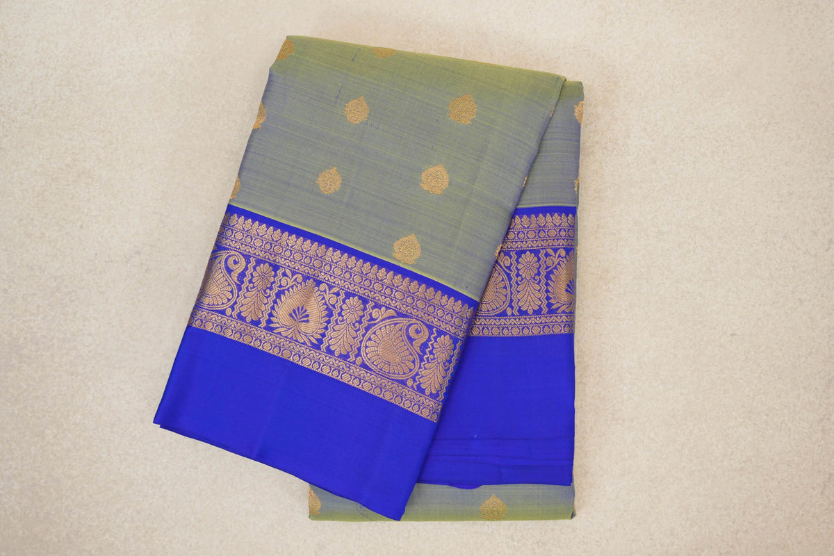 Folded lightweight Kanchipuram silk saree with a yellowish green body, small gold motifs and a royal blue border with gold paisley and floral designs.