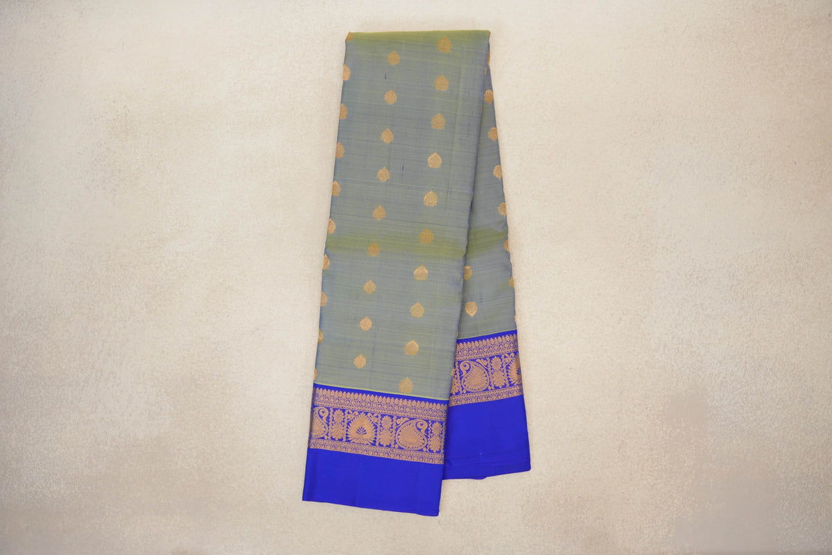 Folded lightweight Kanchipuram silk saree with a yellowish green body, gold teardrop motifs and royal blue borders patterned in gold.