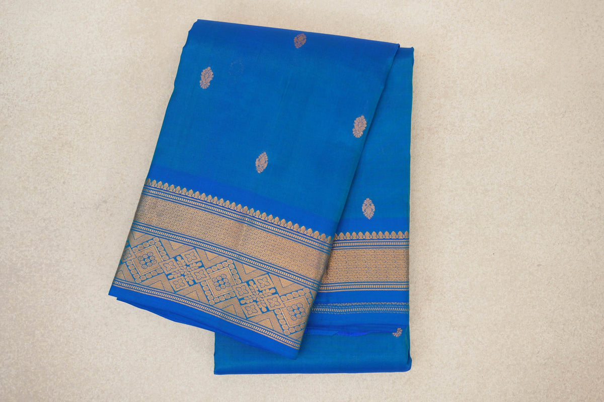 Folded peacock blue light-weight Kanchipuram silk saree with scattered gold motifs and a broad geometric gold border.