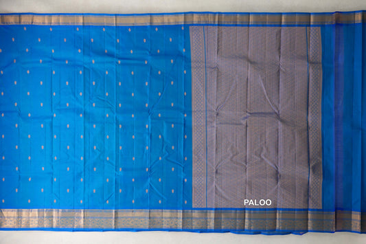 Peacock blue lightweight Kanchipuram silk saree laid open, showing small gold zari accents, patterned borders and a densely woven pallu.