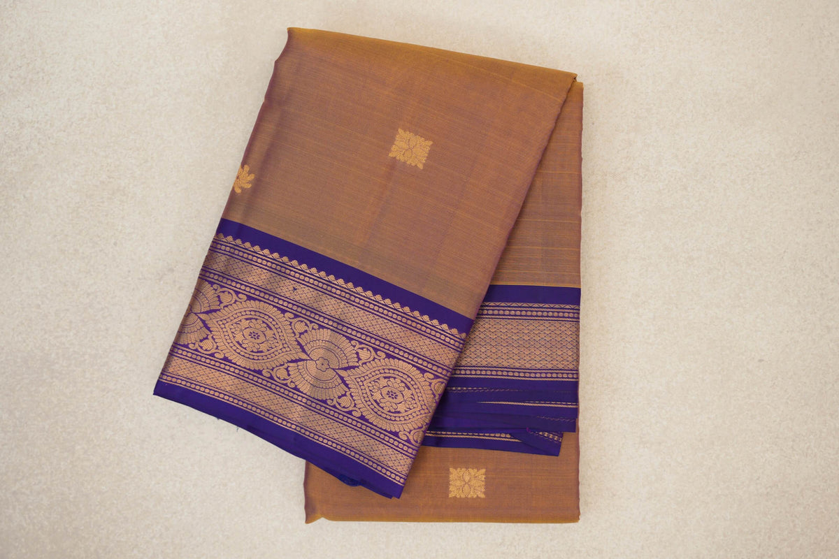 Folded lightweight Kanchipuram silk saree with a muted magenta and yellow body, small gold motifs and a violet purple border with intricate gold patterns.