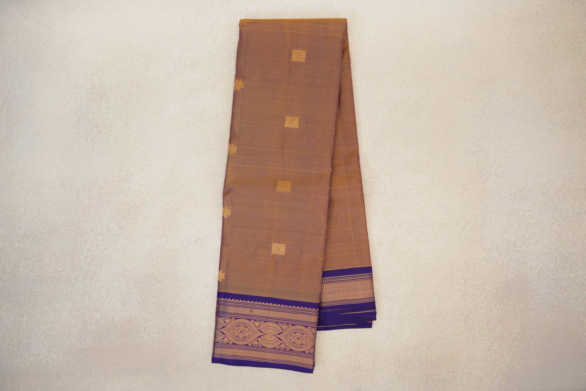 Folded lightweight Kanchipuram silk saree with a muted magenta and yellow body, scattered gold motifs and an ornate violet purple border.