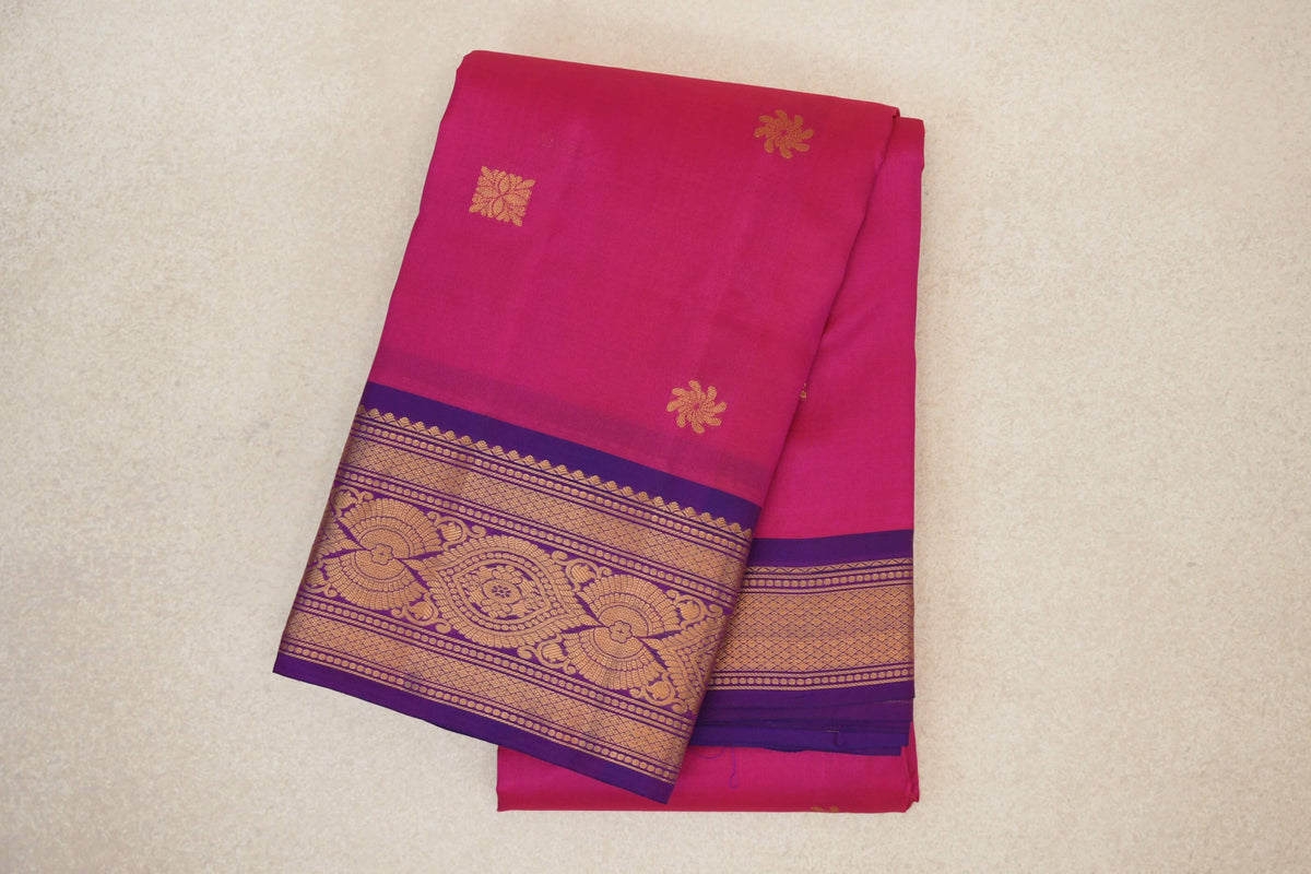 Folded rani pink lightweight Kanchipuram silk saree with scattered gold floral motifs and an ornate gold-patterned magenta purple border.