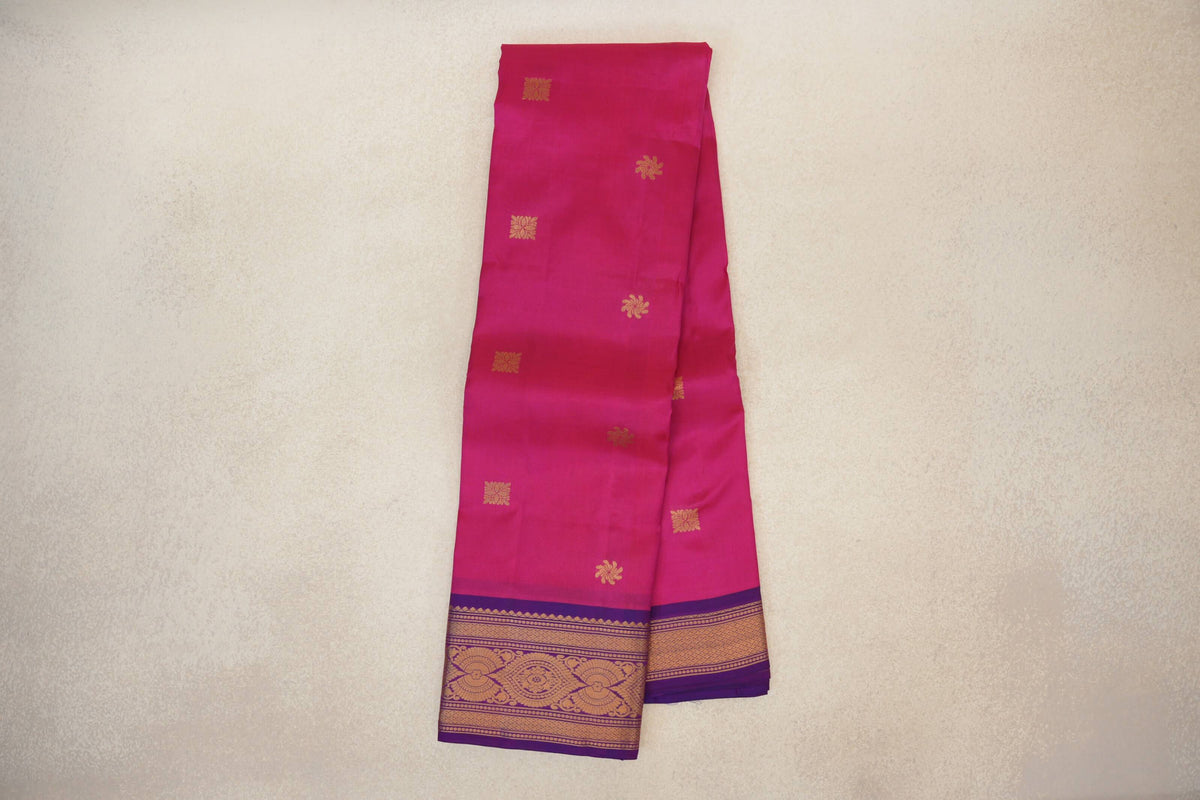Folded rani pink lightweight Kanchipuram silk saree with scattered gold motifs and magenta purple borders with intricate gold designs.