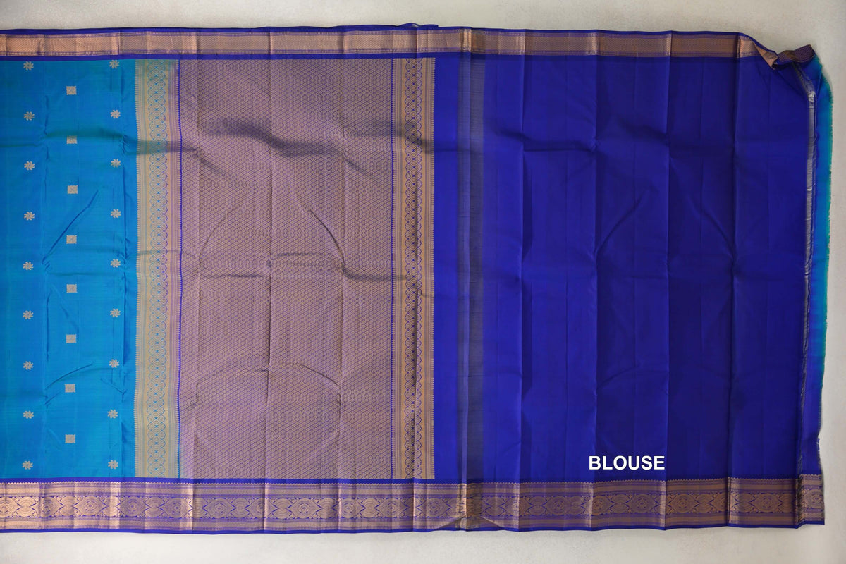 Lightweight Kanchipuram silk saree spread flat, showing a peacock blue body with small gold motifs, a lattice-patterned pallu, ornate borders and a deep royal blue blouse.