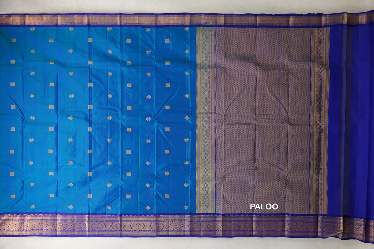 Lightweight Kanchipuram silk saree spread out, with a peacock blue body dotted with gold motifs, deep royal blue borders and a patterned pallu.