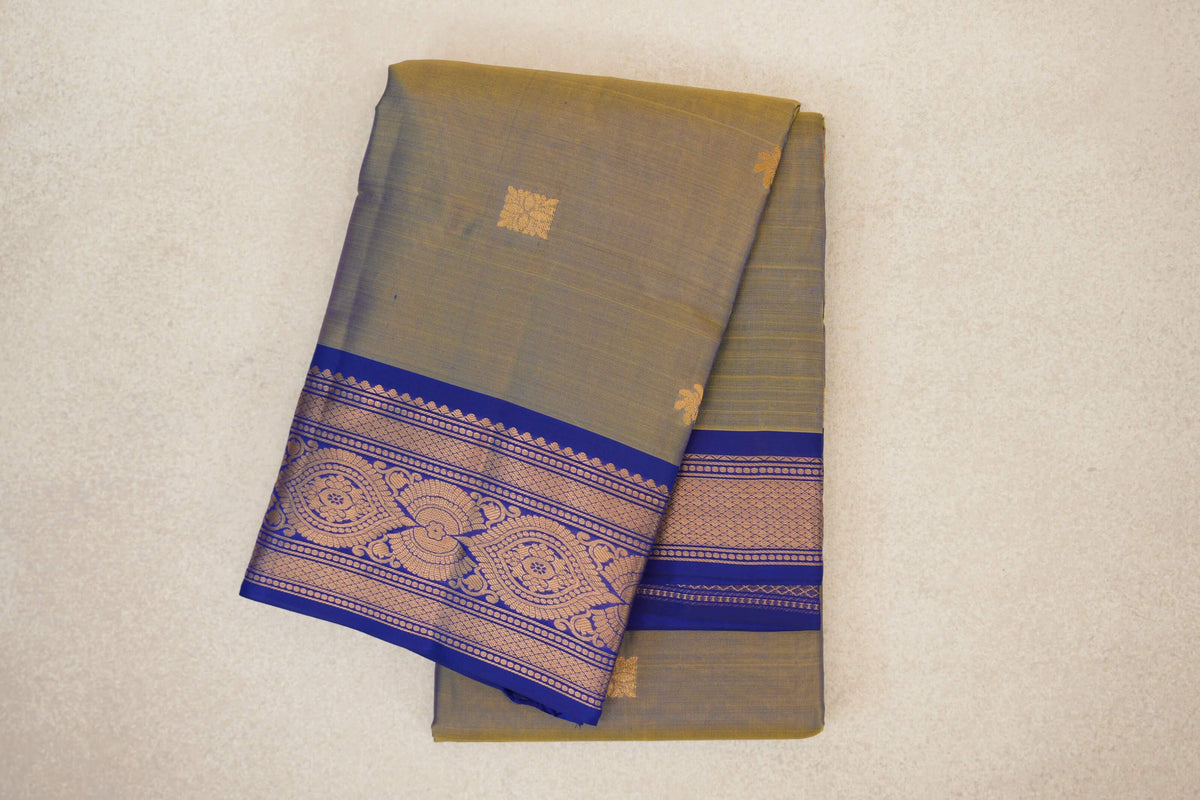 Folded lightweight Kanchipuram silk saree with a muted yellow and violet body, small gold motifs, and an ornate deep royal blue border.