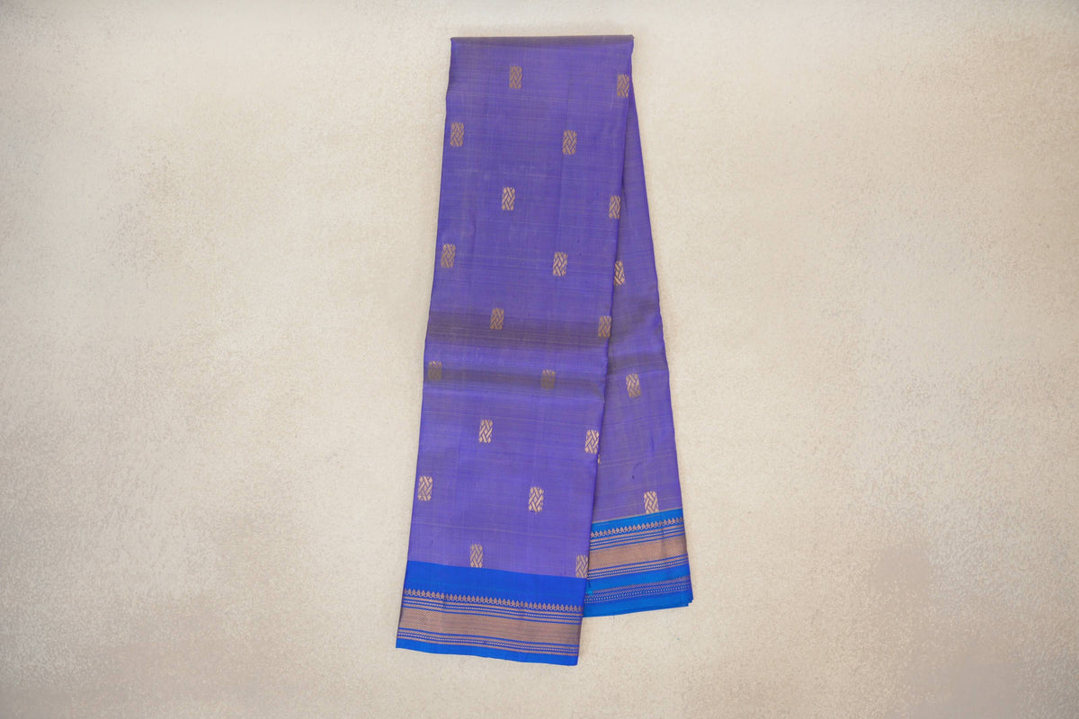 Folded lightweight Kanchipuram silk saree with a lavender body, small gold geometric motifs and royal blue borders with gold-patterned stripes.