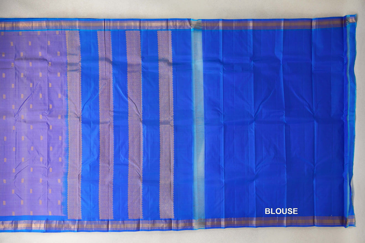 Lightweight Kanchipuram silk saree laid flat, showing a lavender body with small gold motifs, a royal blue pallu with patterned gold stripes, and a royal blue blouse section.