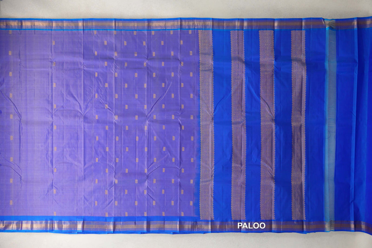 Lightweight Kanchipuram silk saree spread flat, with a lavender body dotted with gold motifs, royal blue borders and a pallu with gold patterned bands.