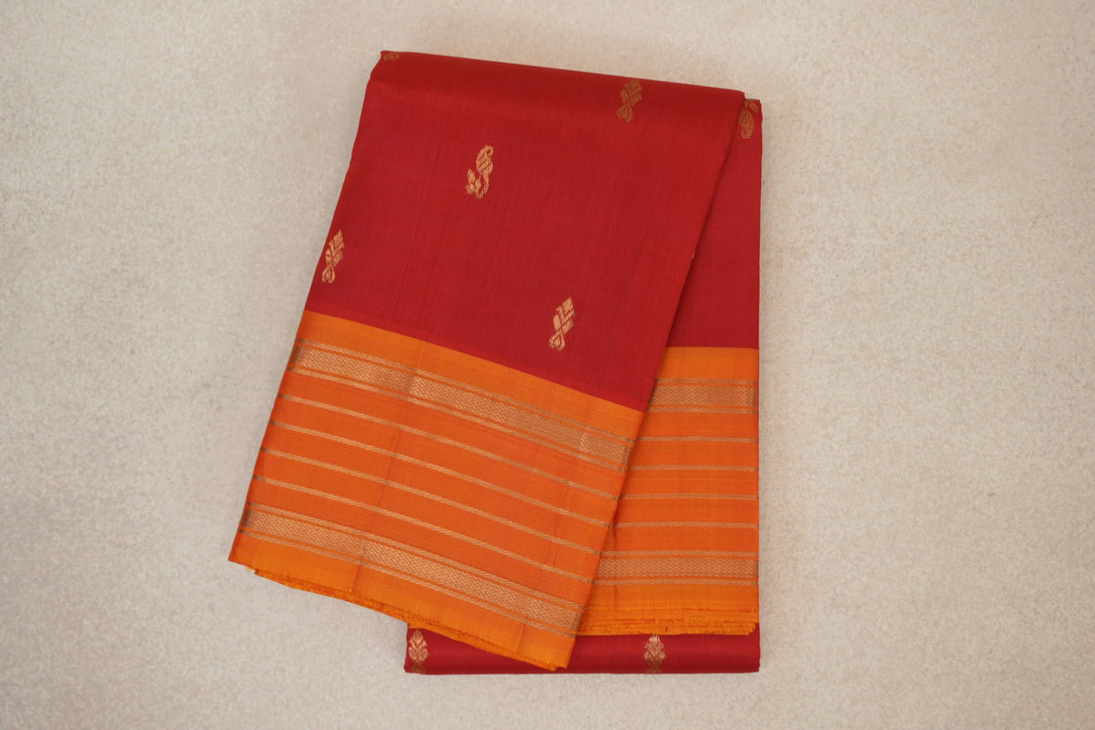 Folded vermilion red Kanchipuram silk saree with small gold motifs and deep orange borders striped in gold.