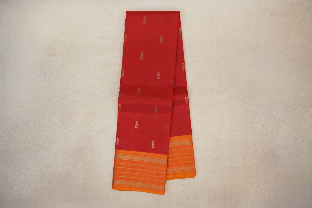 Folded vermilion red light weight Kanchipuram silk saree with scattered gold motifs and deep orange borders with fine gold stripes.