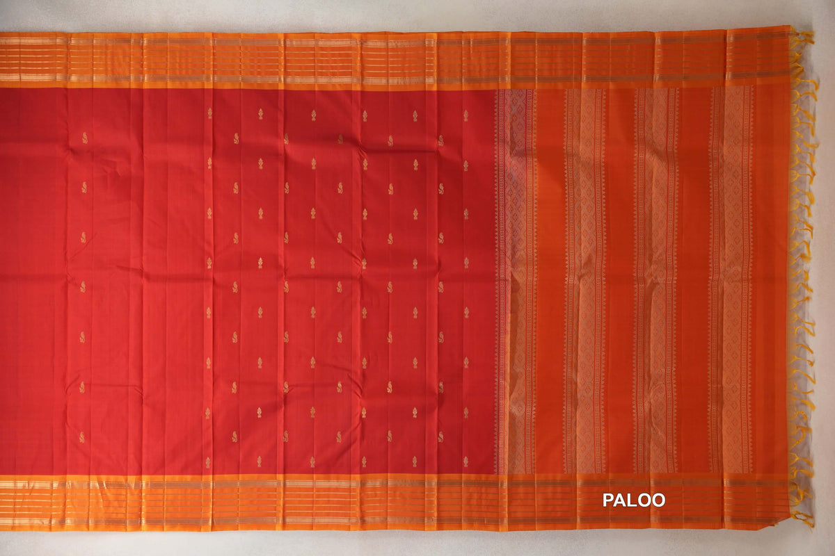 Lightweight Kanchipuram silk saree spread flat, with a vermilion red body dotted with small gold motifs, deep orange striped borders and a patterned pallu with tassels.