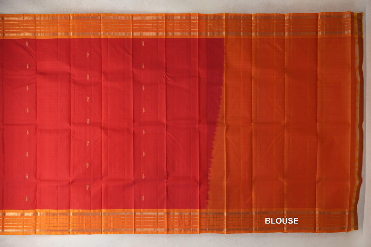 Light weight Kanchipuram silk saree laid flat, with a vermilion red body dotted with small gold motifs, deep orange striped borders and a matching blouse panel.