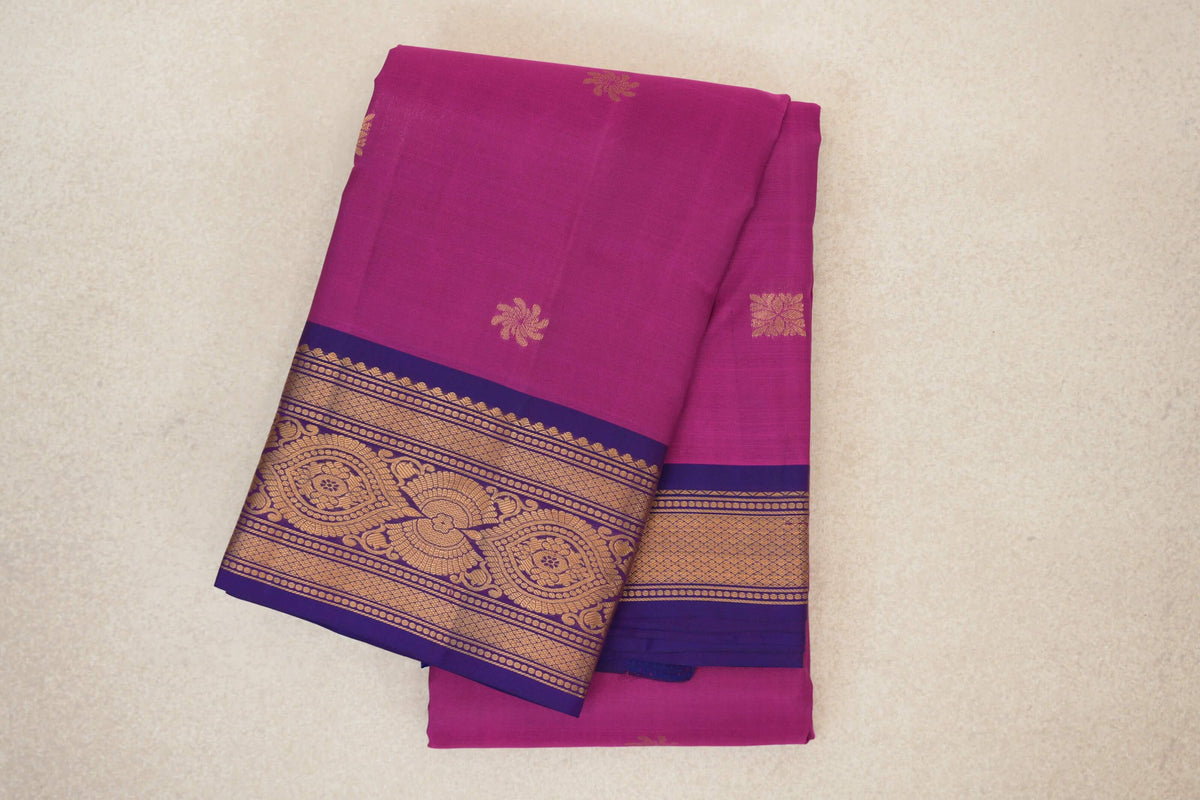 Folded deep magenta Kanchipuram silk saree with small gold motifs and violet purple borders woven with ornate gold designs.