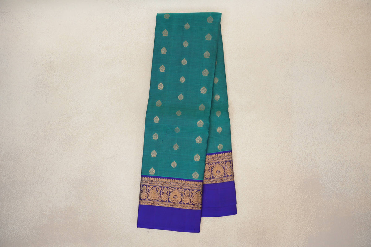 Folded peacock green lightweight Kanchipuram silk saree with small gold motifs and deep royal blue borders patterned with gold paisleys and flowers.